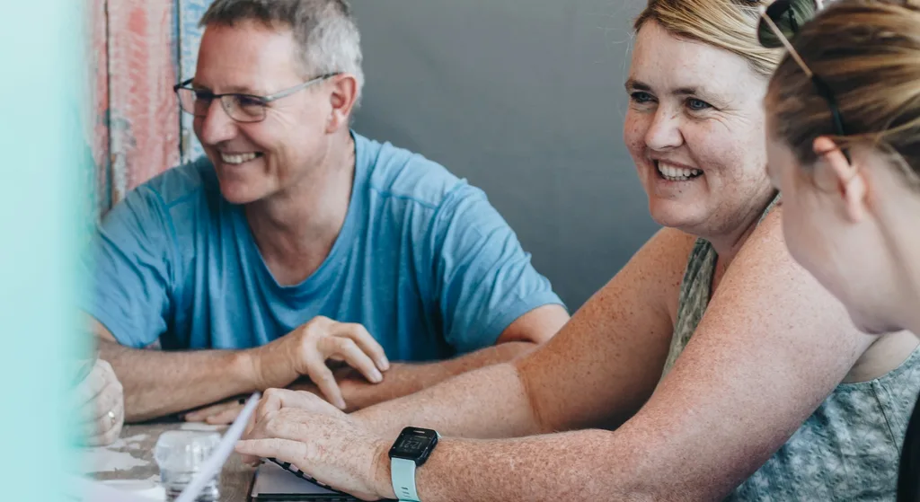 Three adults laughing together while gathered around an outdoor table